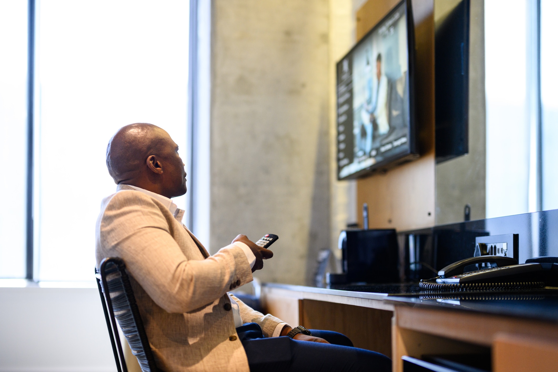 Side view of a man in casual business attire sitting in front of a flat screen television in a hotel room,