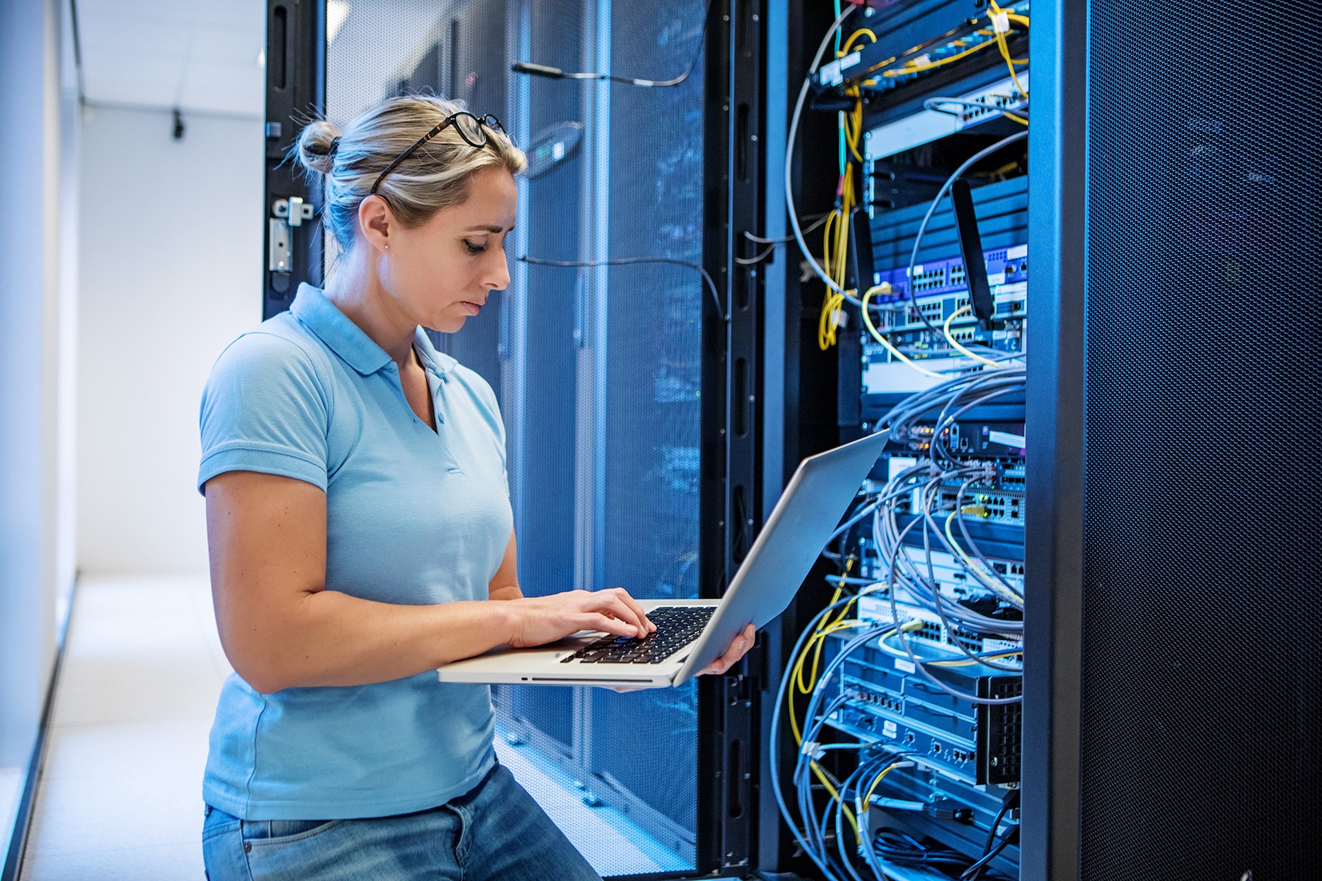 A woman with a silver laptop working in a server room